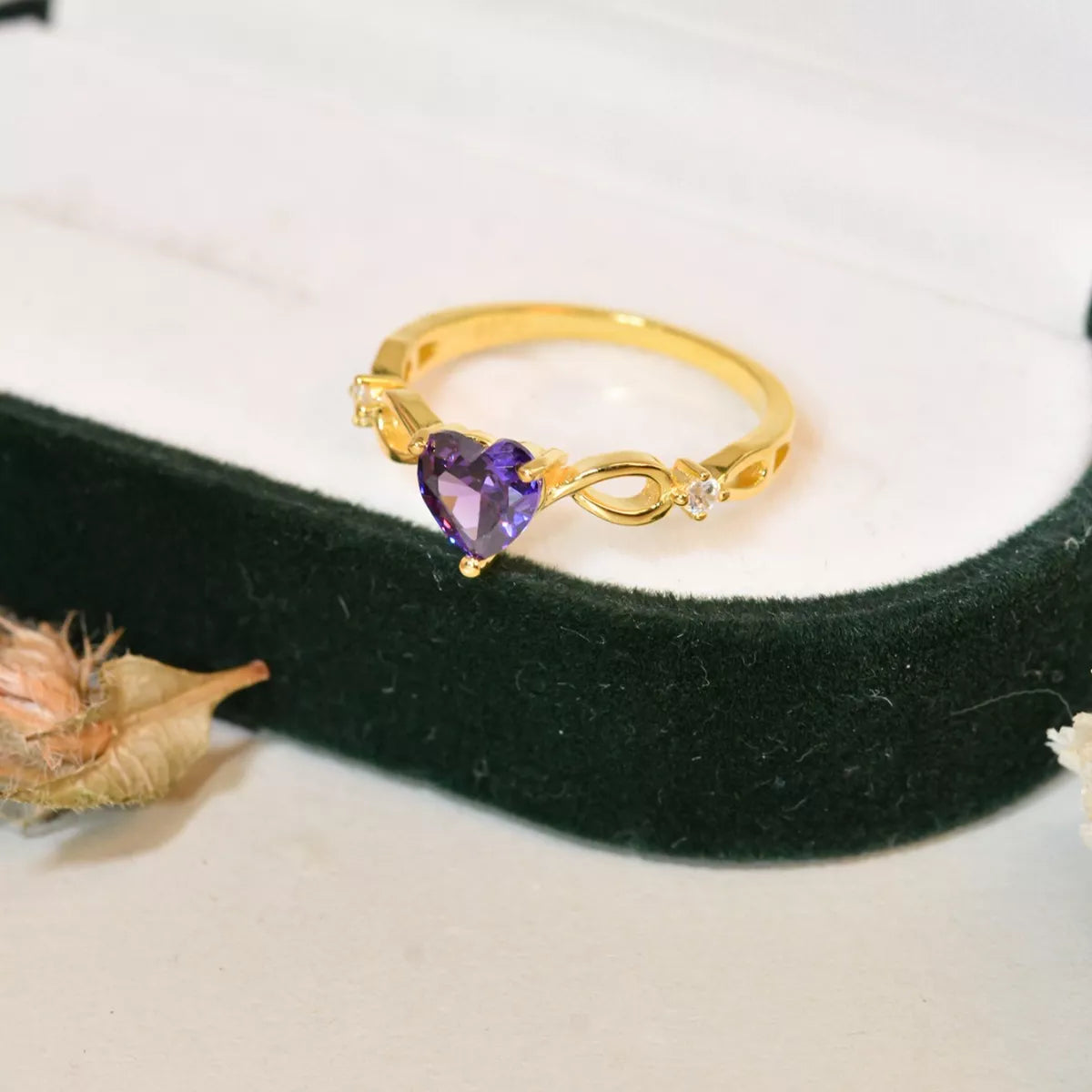 Close-up of gold ring with heart-shaped amethyst gemstone on dark green velvet jewelry box