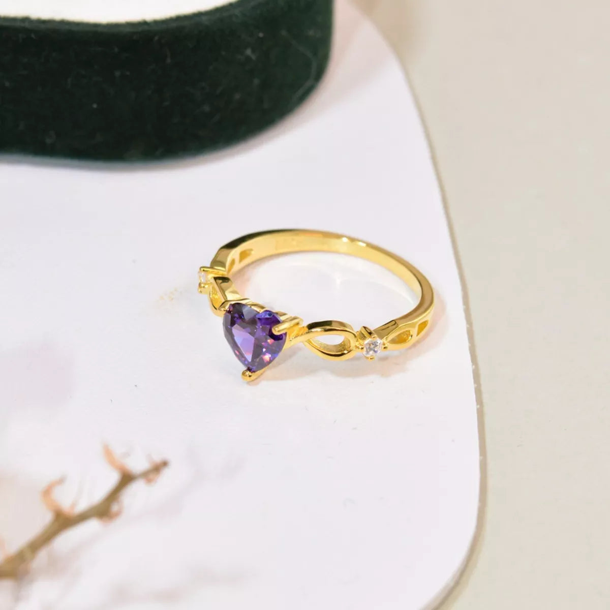 Gold ring with heart-shaped purple amethyst gemstone on white surface beside green jewelry box