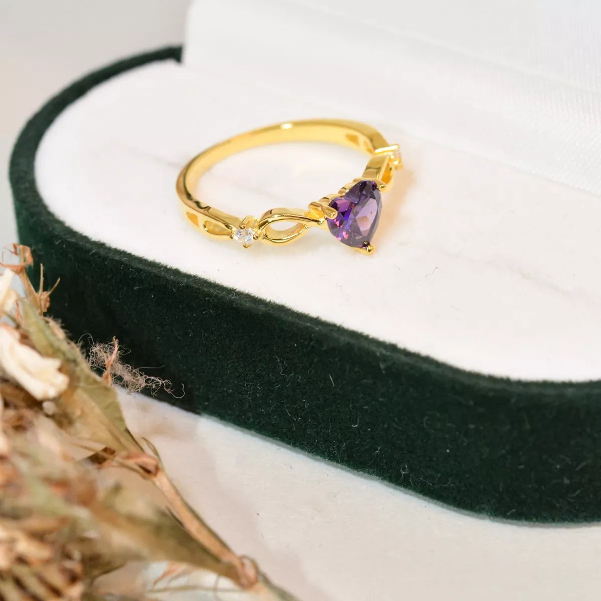 Gold ring with heart-shaped purple amethyst gemstone photographed from the side on a green velvet jewelry box