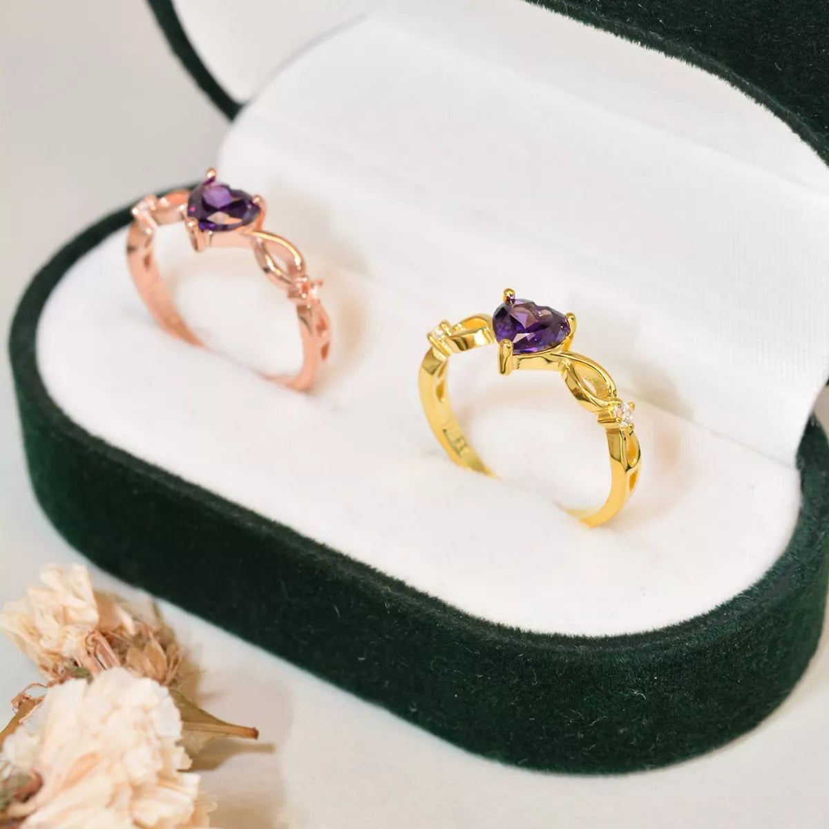 Gold and rose gold amethyst heart rings displayed together in a dark green velvet jewelry box