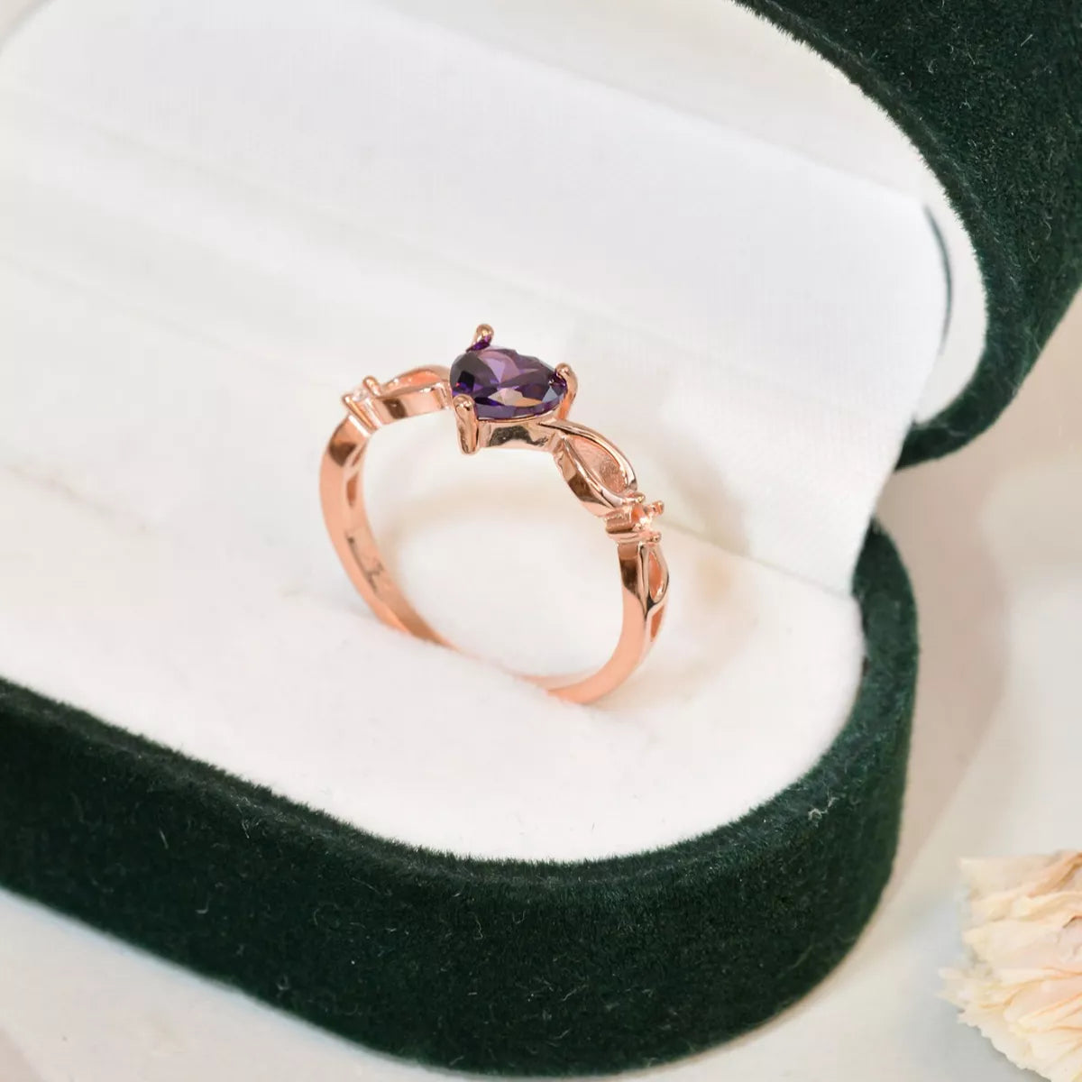 Rose gold ring with heart-shaped amethyst gemstone displayed in a green velvet jewelry box