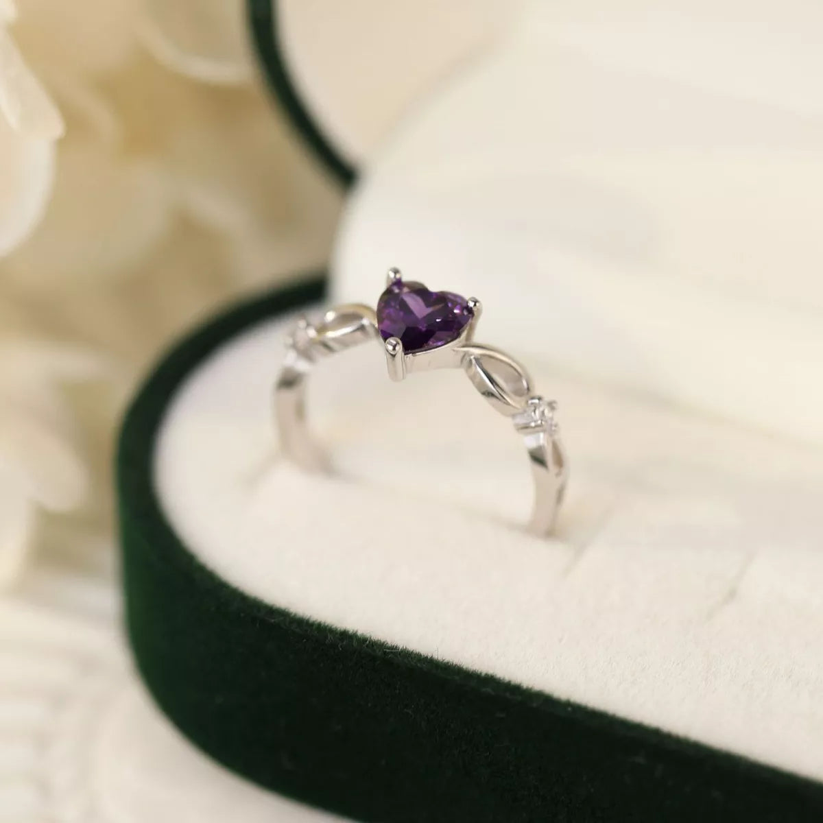 Side view of silver ring with heart-shaped amethyst gemstone in green velvet jewelry box