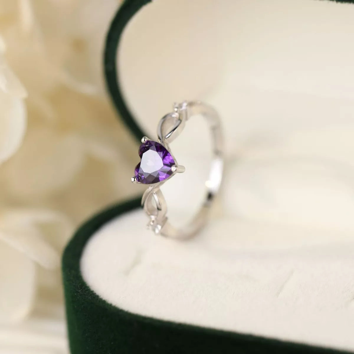 Top view of a silver ring featuring a heart-shaped purple amethyst gemstone on white velvet background