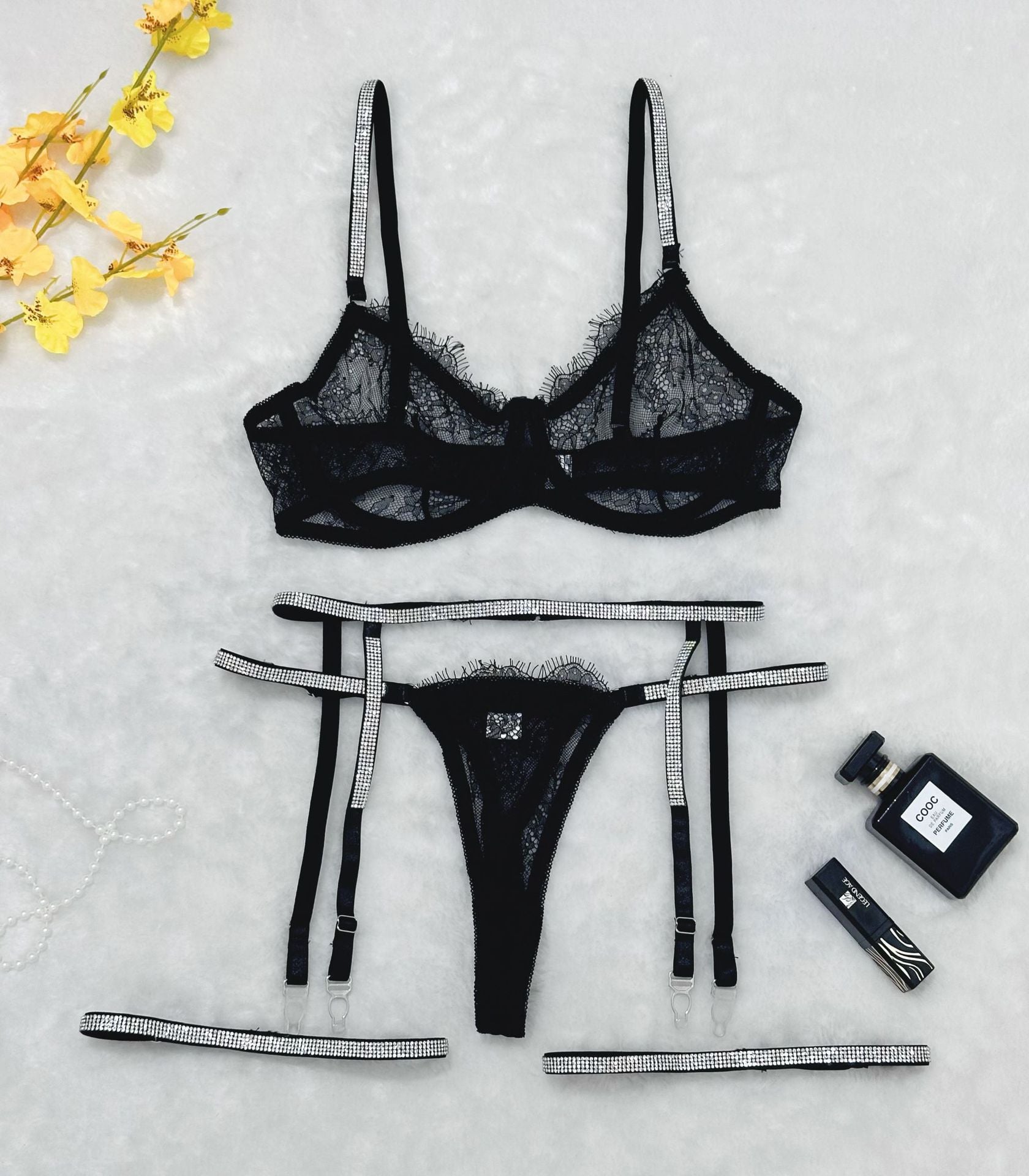 Flat lay of black lace lingerie set with rhinestone straps, garter belt, and thong