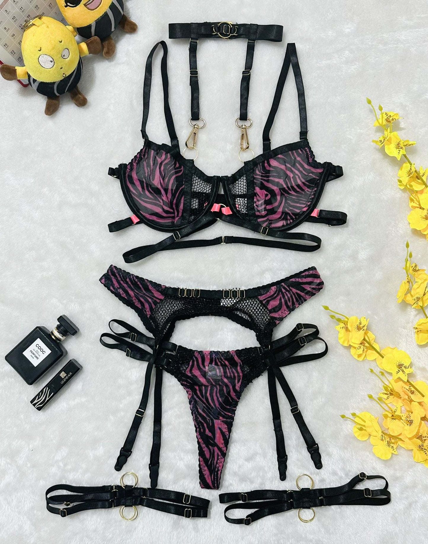 Flat lay of black and pink zebra print harness lingerie set with gold rings and mesh details