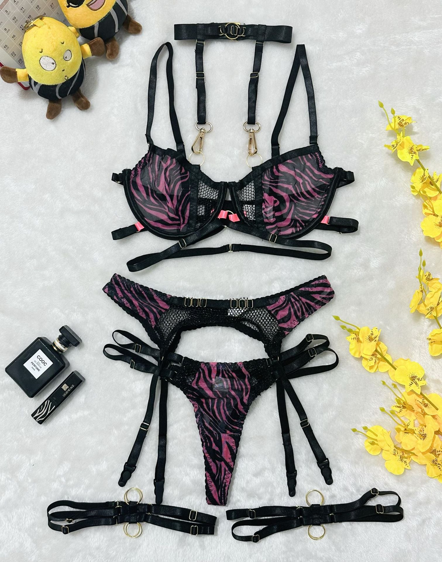 Flat lay of black and pink zebra print harness lingerie set with gold rings and mesh details