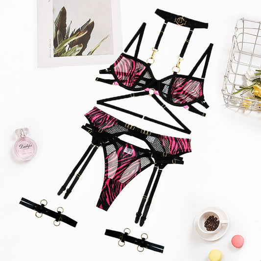 Flat lay of black and hot pink zebra lace strappy lingerie set with gold hardware and garter belt