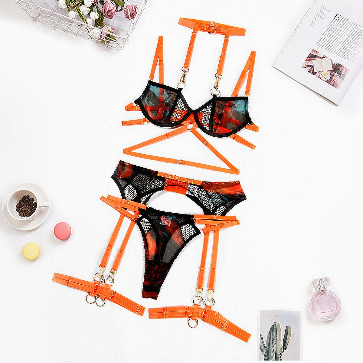 Flat lay of orange and black sheer mesh lingerie set with gold rings and garter straps