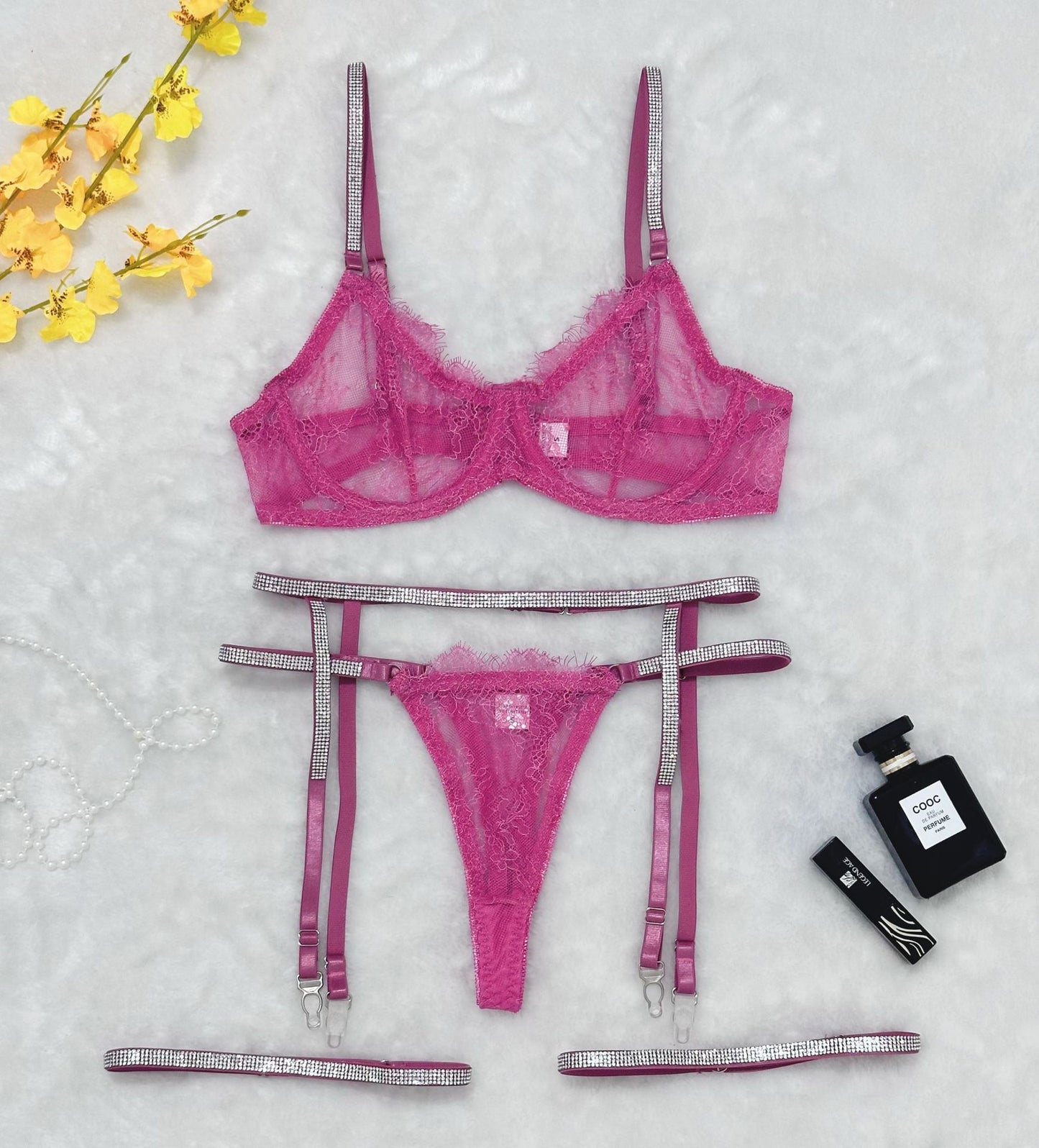Flat lay of pink lace lingerie set with rhinestone straps, garter belt, and thong
