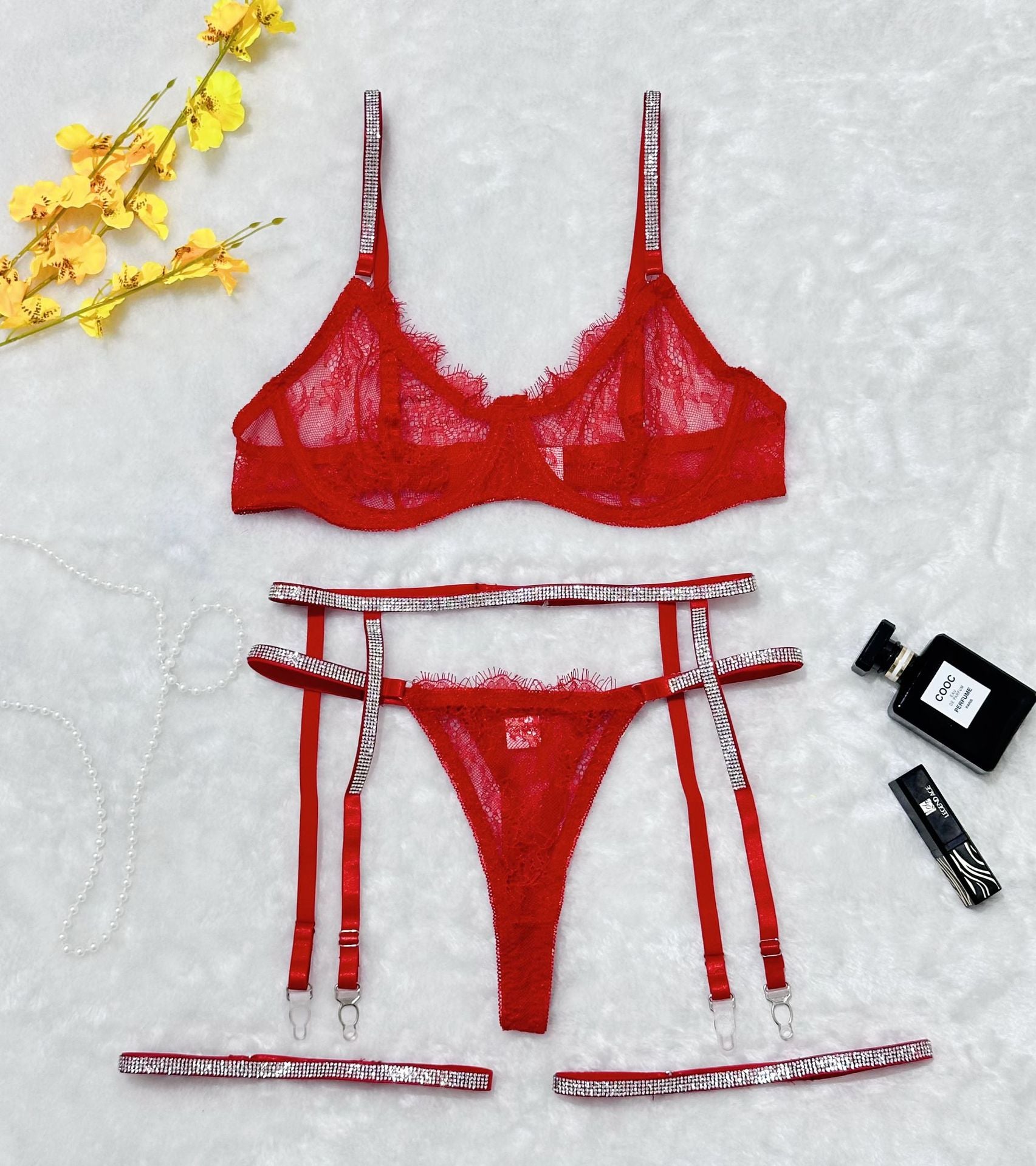 Flat lay of red lace lingerie set with rhinestone straps, garter belt, and thong
