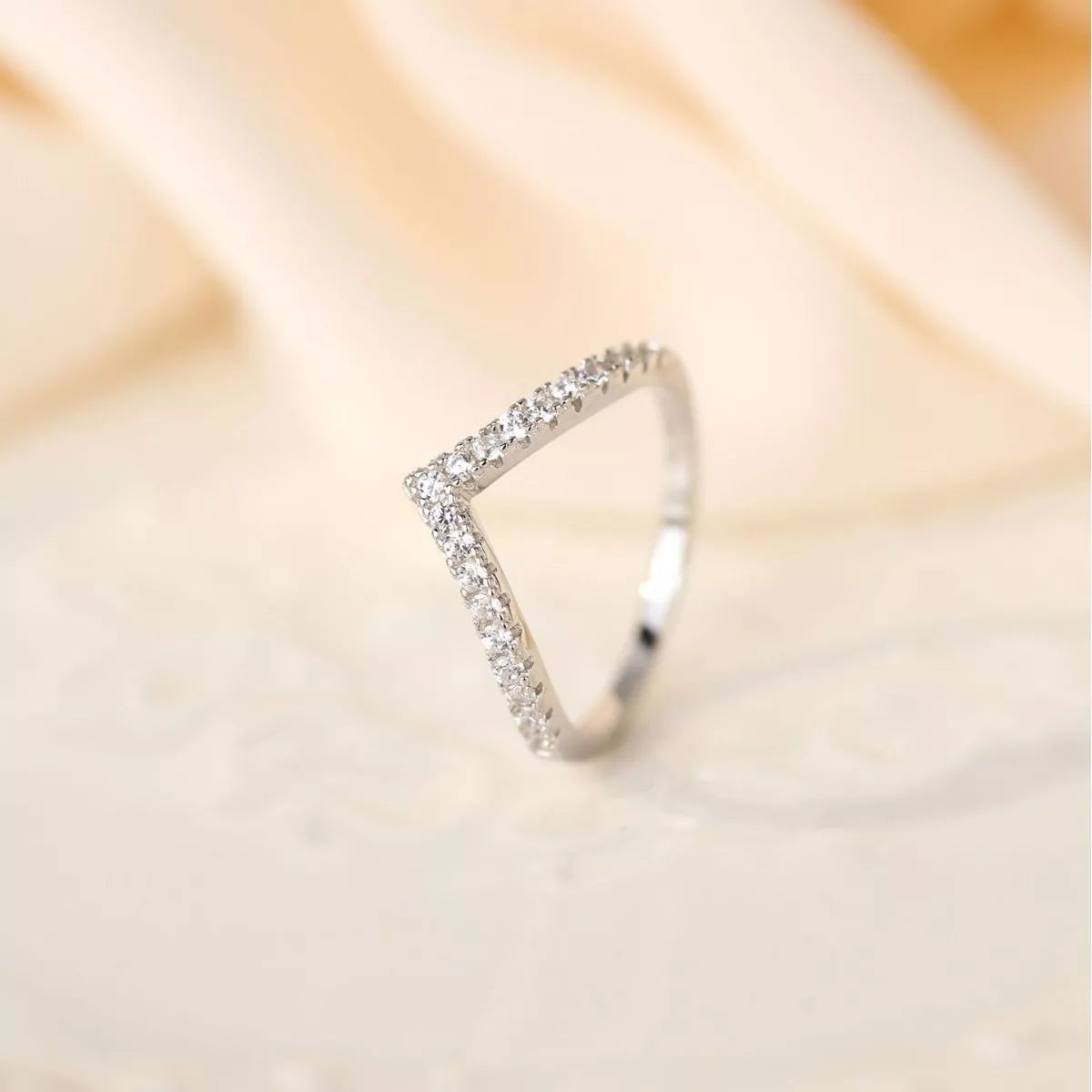 V-shaped sterling silver ring with pavé-set diamonds on a soft beige background
