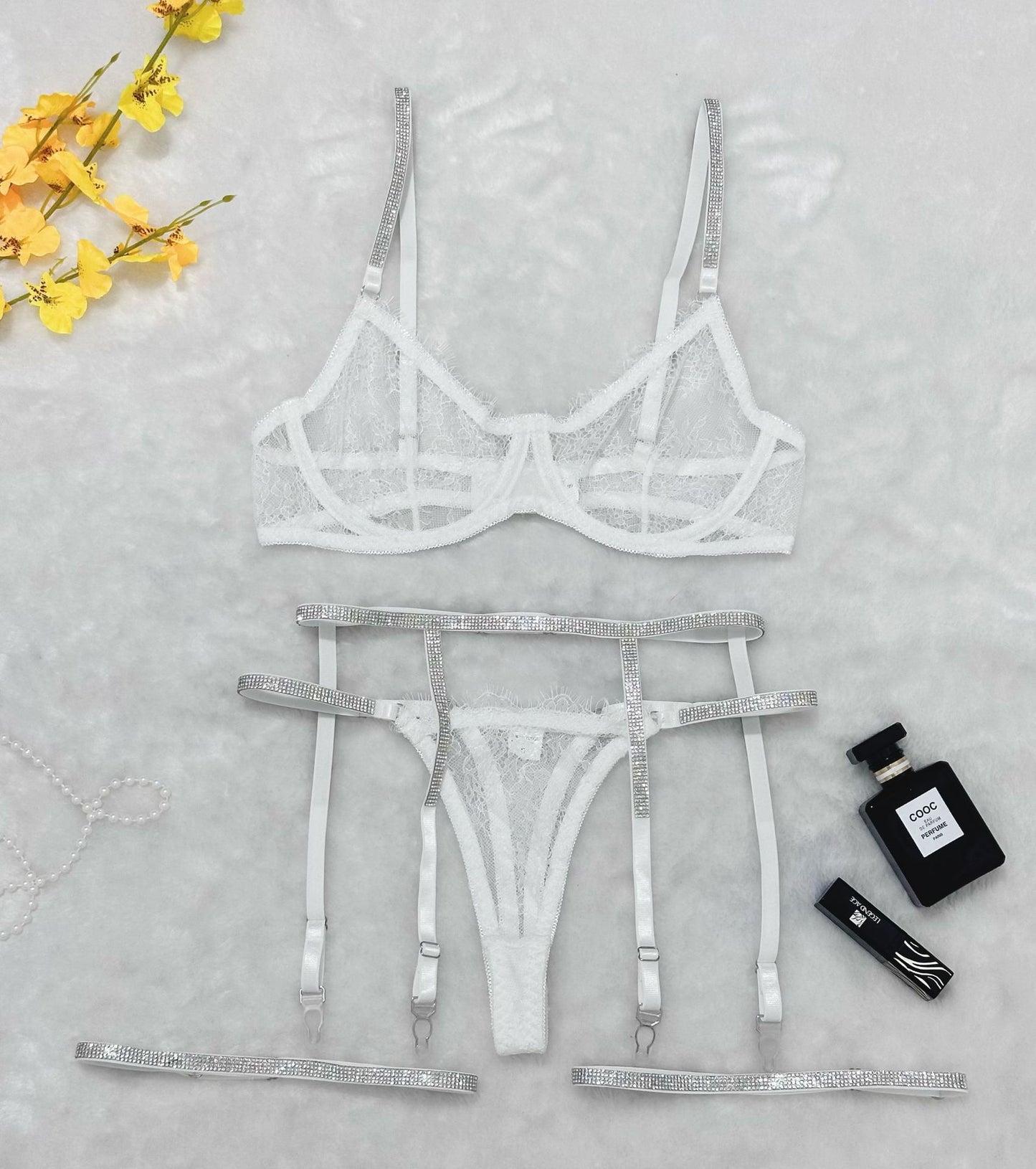 Flat lay of white lace lingerie set with rhinestone straps, garter belt, and thong